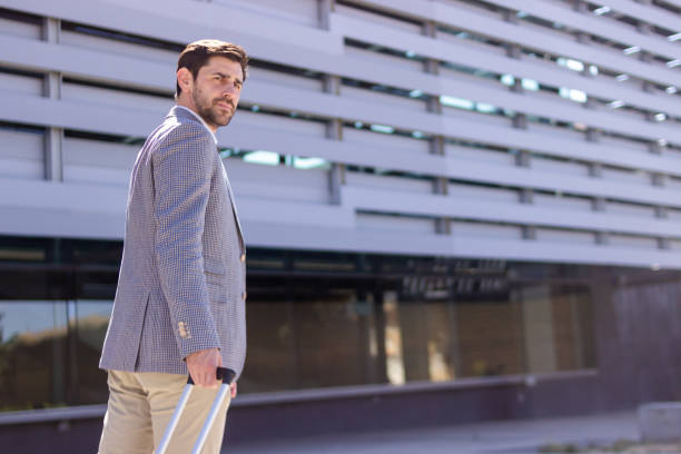 istock Businessman walking with suitcase in front of modern building 2160422097