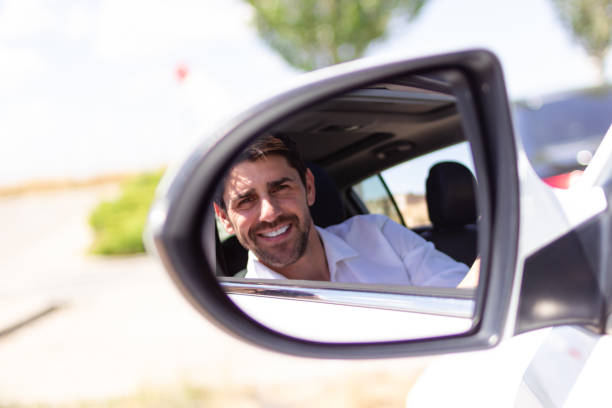 istock Businessman smiling and driving car while looking in rearview mirror 2160423271