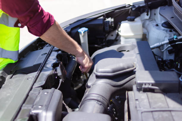 Auto mechanic wearing reflective vest checking engine oil level with dipstick