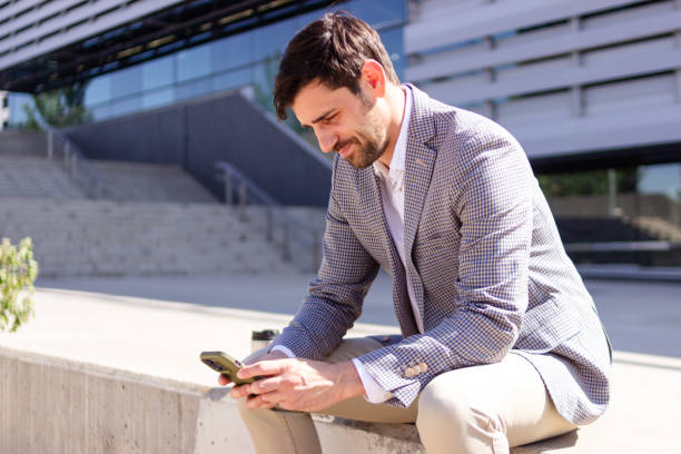istock Businessman using smartphone sitting outside modern office building 2160423688