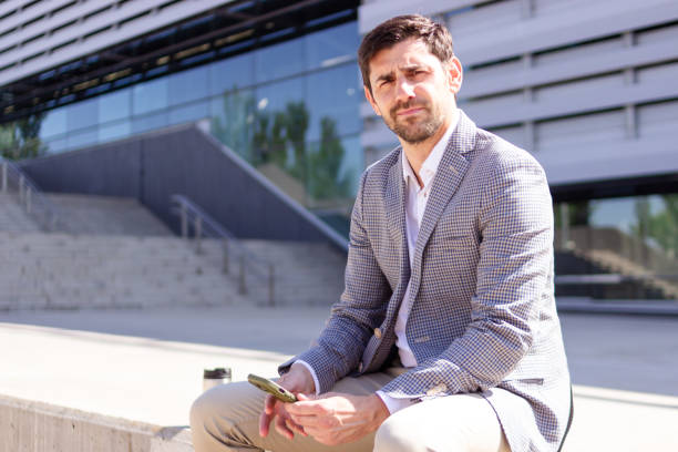 istock Businessman sitting outside office building using smartphone 2160423707