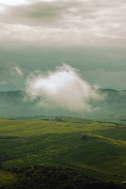 View of the enchanting atmosphere of Tuscany with this captivating scene of fog rolling over green hills on a rainy spring day. The mystical fog and dark weather create a hauntingly beautiful landscape, capturing the unique charm and allure of this iconic Italian region.