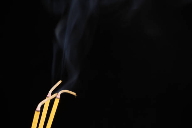 Three yellow incense sticks burning on black background