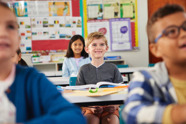 Smiling elementary school kids sitting at desks in classroom. Group of diverse classmates studying in elementary school. Portrait of smiling school boy listening to teacher and attending class at primary school.