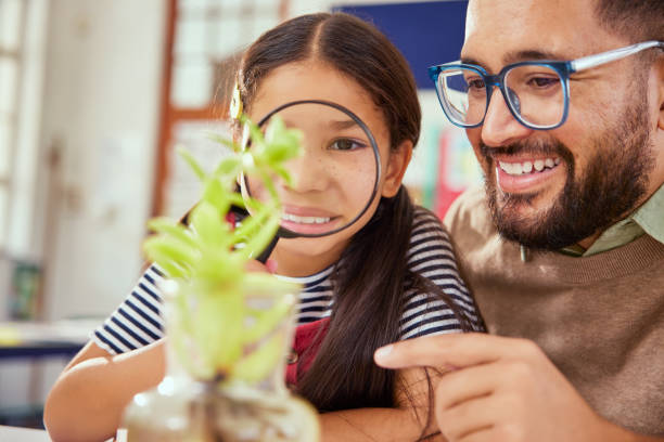 istock Teacher with primary school girl exploring plants with magnifier 2160438239
