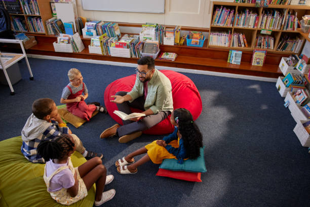 istock Friendly teacher reading a book to pupils during literature class 2160438957