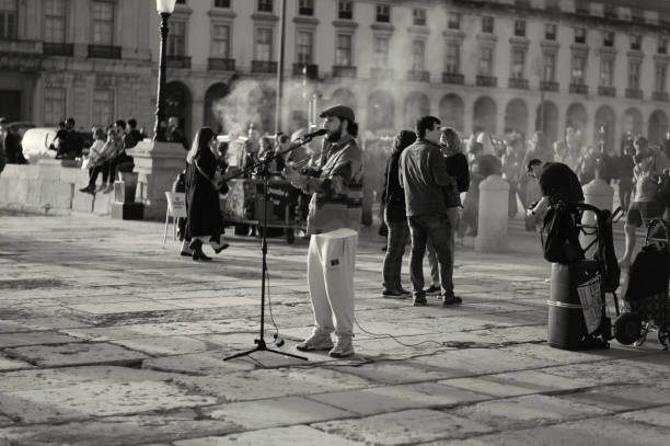 Naples, Italy – March 2018: A man sits alone on the marble ledge at the Piazza Dante metro station in Naples. His hands clasped together, his gaze steady, a small orange bag beside him. Behind the glass, the reflections of the square, a woman on the phone descends the stairs. Everything reflects and blurs, as if in a single urban breath. A silent, real scene, speaking of waiting and daily life in the city.