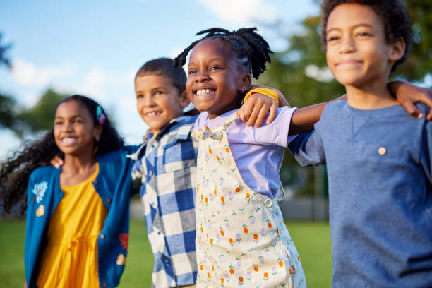 Multiethnic group of children friends enjoy together while hugging Side view of little children jumping together in a row while looking their bright future. Happy little boys and smiling cute girls making friends and having fun together at park. Cheerful multiethnic kids enjoying summertime and embracing in outdoor park at sunset during summer camp. children only stock pictures, royalty-free photos & images