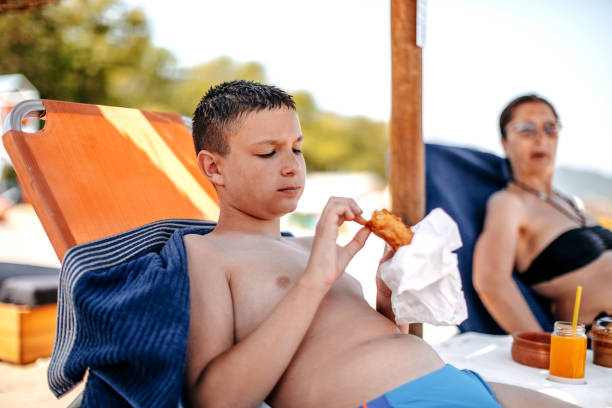 Parent spending time together with teenager son on vacation on the beach eating under parasol