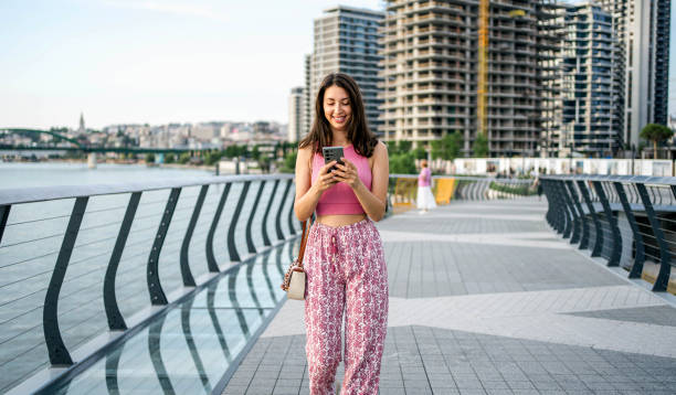 istock Young woman using phone while walking by the river 2160461751