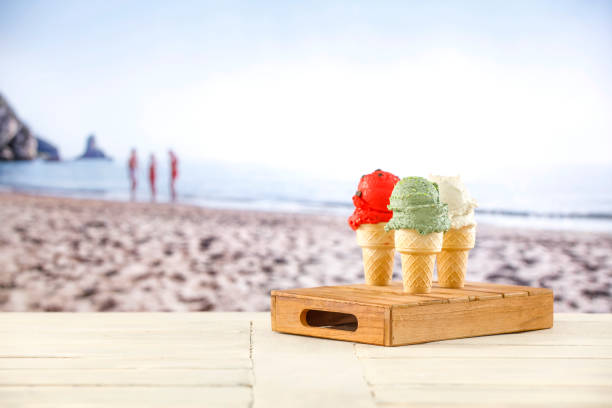 Ice cream in waffle cones on wooden cafe beach table with blurred beach background. Summer image and table background with copy space for products.