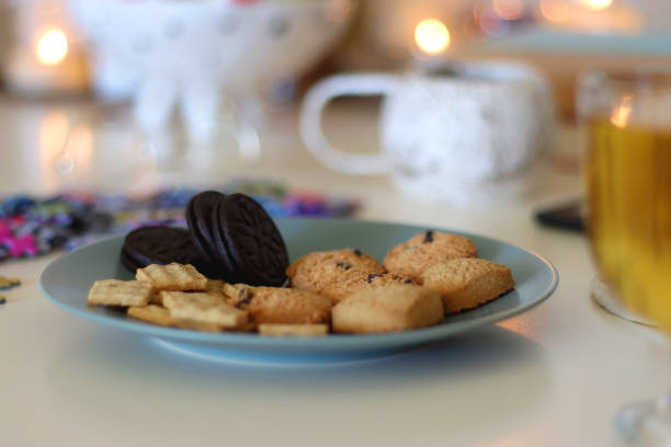 Colorful jigsaw puzzle pieces, books, tablet, glasses, cookies, berries, cup of tea or coffee, glass of juice and lit candles on the table. Hygge in pastel colors. Selective focus.