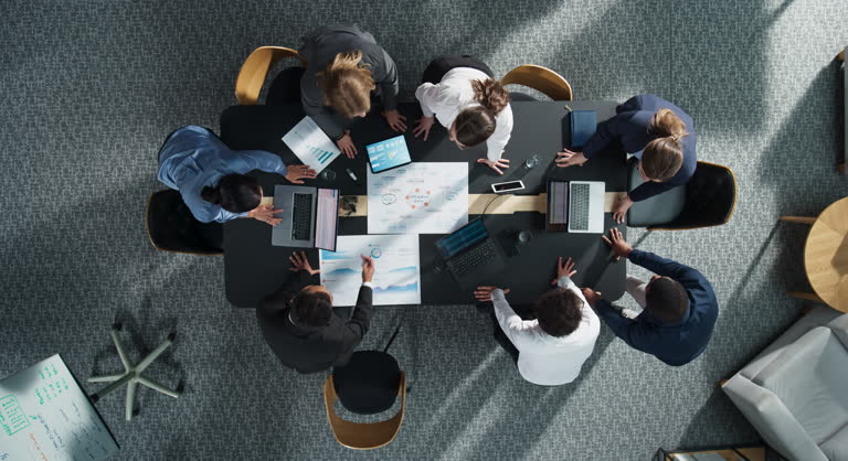 Zoom Out Top Down View: Diverse Team Of Business Professionals With Laptops Entering The Conference Room And Sitting Behind Table To Discuss Financial Data And Project Mindmap in Corporate Office.