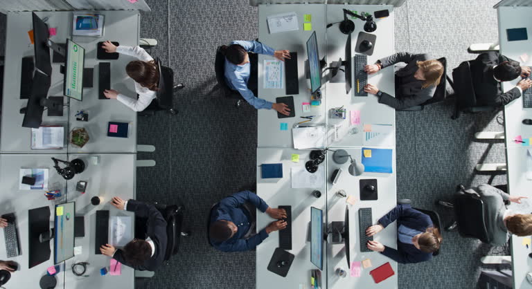 Top Down View of Multiethnic Team in a Corporate Office, Working on Desktop Computers And With Financial Documents. Colleagues Working Creating Reports, Developing Business Strategies For Hedge Fund.