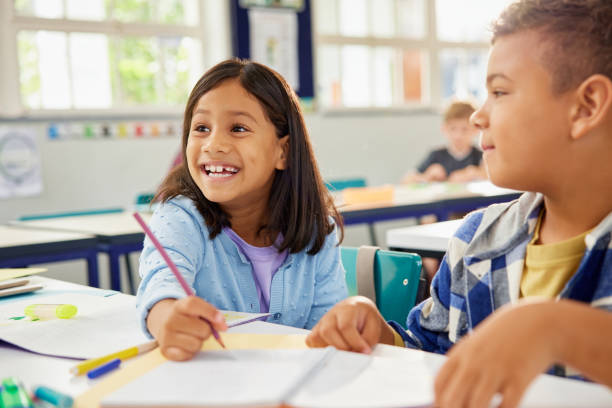Happy smiling school girl helping classmate in classroom Cheerful and helpful middle eastern schoolgirl assisting classmate in studies during lesson. Cute girl and school boy studying together in classroom in school. Indian child working together with friend for a group task. elementary student stock pictures, royalty-free photos & images