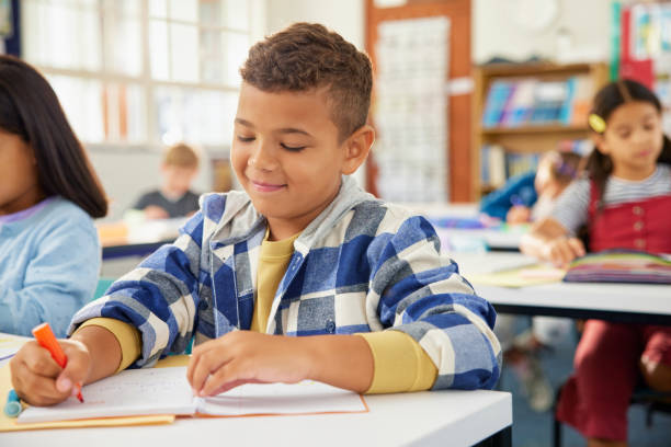istock Mixed race school boy writing in primary classroom during test 2160474583