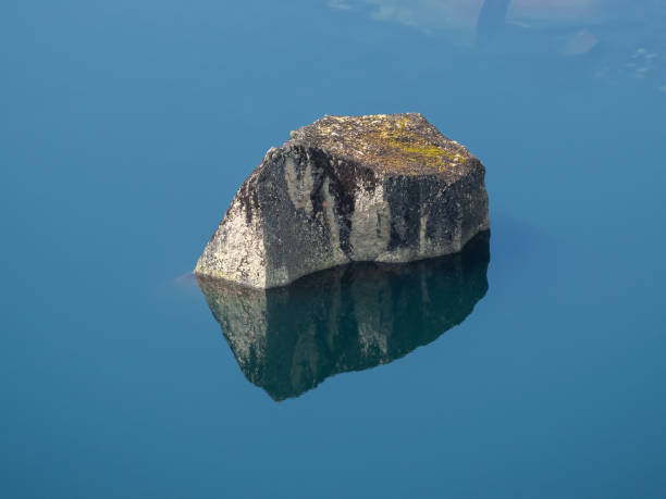 Huge boulder in the lake, stone reflection in still clear blue water. Clear mountain lake with a stone.