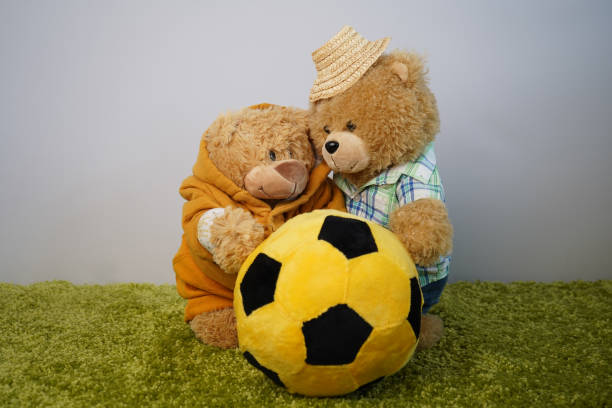 Two teddy bears in a tender relationship play yellow ball.