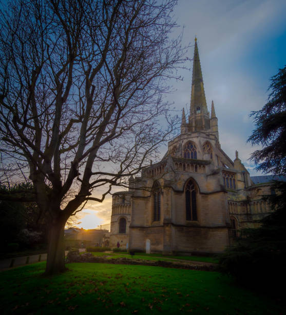 Norwich Cathedral from the graveyard in a golden sunset beneath bare winter trees