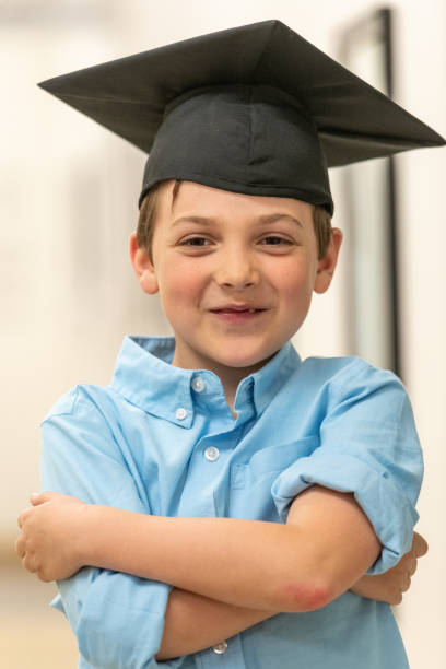 Smiling caucasian little boy wearing a graduation mortar hat looking at the camera