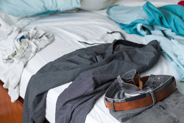 Pants, pajamas and T-shirt scattered on the bed. Crumpled sheets and scattered pillows