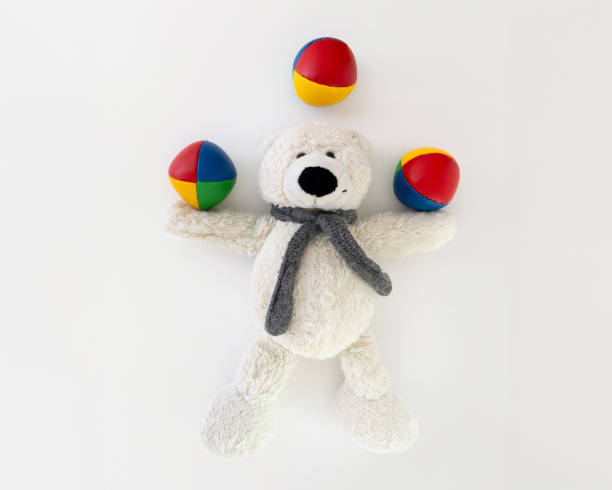 This charming scene features a cute teddy bear surrounded by three colorful balls on a white background, captured from a top view. The ample space for text makes the image ideal for design projects requiring text overlay. Perfect for nursery decoration, educational materials, or toy advertisements. An image that conveys joy and creativity