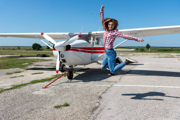 A young female pilot jumps for joy in front of her small plane.