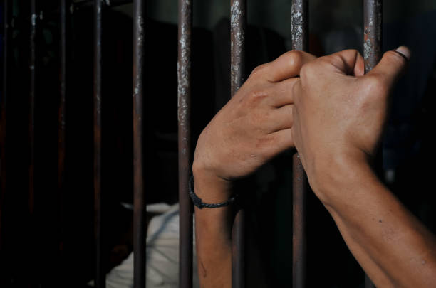 istock hands of a prisoner behind prison bars on black background 2160520979