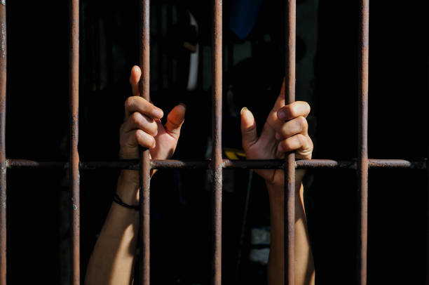 istock hands of a prisoner behind prison bars on black background 2160520983