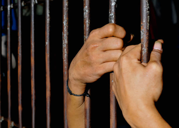 istock hands of a prisoner behind prison bars on black background 2160520987