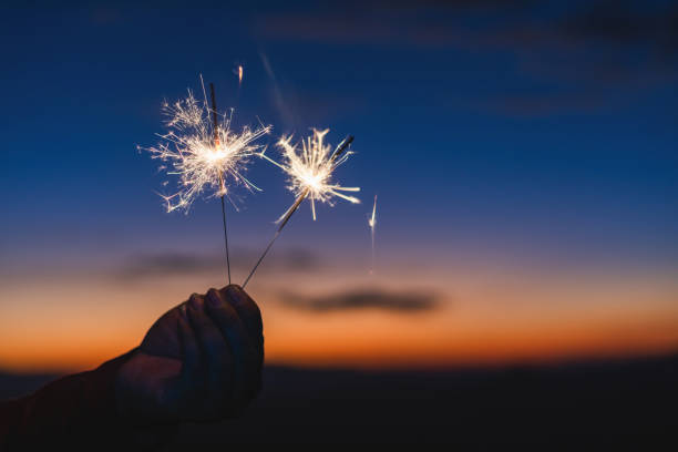 istock Hand holding beautiful sparkler burning and emitting bright sparks on sunset background 2160522433
