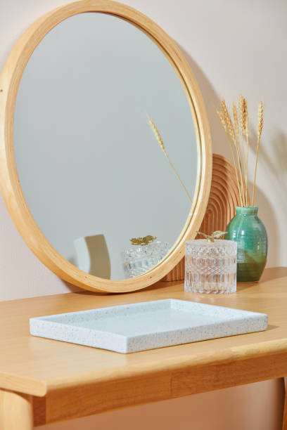 istock A large empty tray in white color displayed on a wooden table, behind it is decorated with a big mirror, a glass pot and a flower vase. Photo has diagonal angle, copy space for text 2160522493