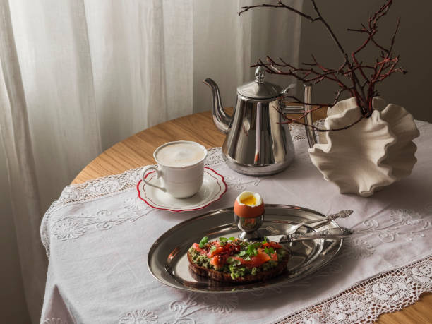 istock Aesthetic breakfast served, brunch - toast with avocado and salmon on rye bread, boiled egg, coffee on a wooden round table in the living room 2160526991