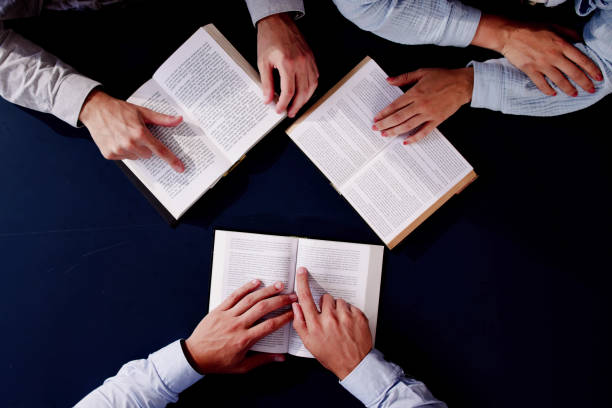 istock Man studying Bible with friends at high desk in background 2160535149
