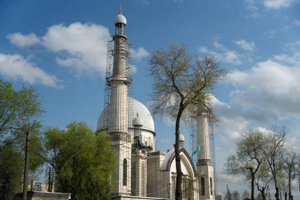 A large white building with a dome on top. The building is surrounded by trees and has a blue sky in the background