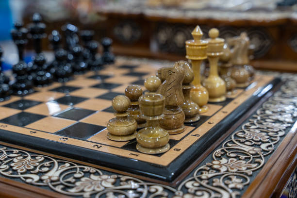 A wooden chess set with a black and white checkered board. The pieces are made of wood and are arranged in a game of chess