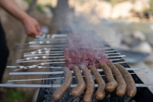 A person is cooking meat on a grill. The meat is being cooked on skewers and there are several pieces of meat on the grill