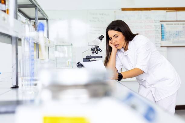 istock Scientist in lab coat leaning on desk by microscope. 2160539041