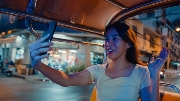 istock Young Asian woman backpack using mobile phone make vlog and live in social media while inside a Tuk Tuk vehicle on the street at Bangkok, Thailand. Holiday vacation trip. 2160541181