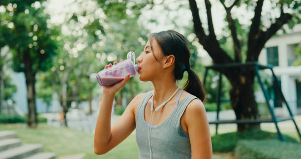 Young Asian female athlete runner drinking protein shake after exercise workout in urban park. Diet and healthy food workout exercise.