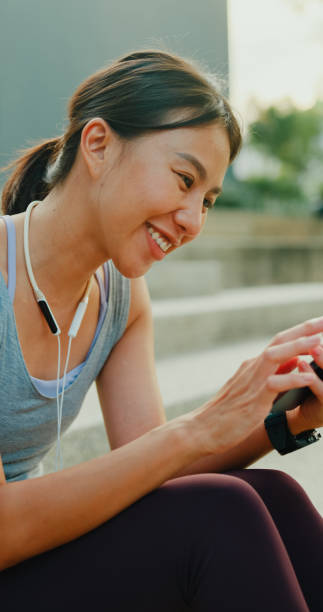 istock Young Asian female athlete runner drinking protein shake and using smartphone after exercise workout in urban park. Diet and healthy food workout exercise. Vertical Screen. 2160543144
