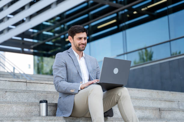 istock Businessman sitting on stairs using laptop outside office building 2160545009