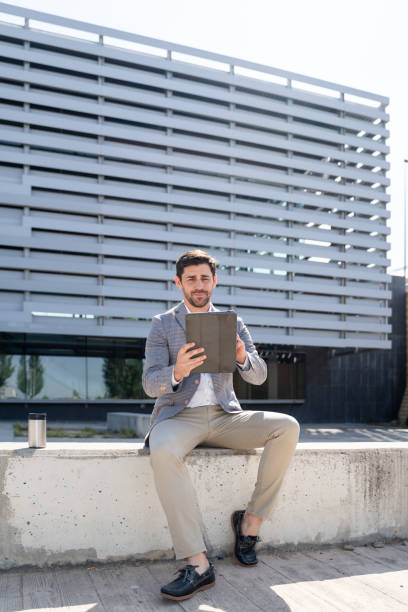 istock Businessman sitting outside modern office building using digital tablet 2160545094