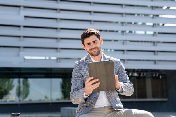 istock Businessman sitting outside office building using digital tablet 2160545115