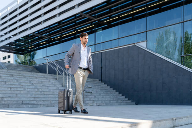 istock Businessman walking with suitcase in front of modern office building 2160545303