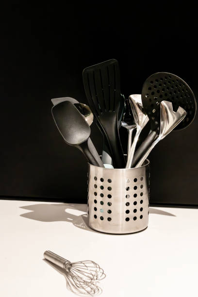 istock Kitchen utensils in containers in kitchen. Strainer Spoon, Spaghetti Server, Slotted Tourner, Salad Fork Spoon, Spatula, Metallic Spoon against black and white background. 2160545398