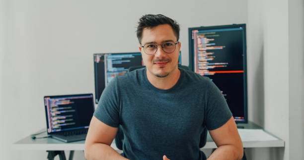 istock Young man software developers for AI technology smiling and looking at camera sitting at desk with multiple screens work at home office. Programmer development. 2160545448
