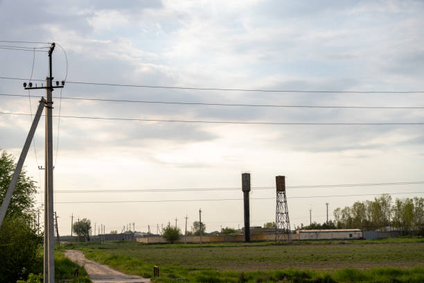 A rural area with a power line pole and a few other poles. The sky is cloudy and the sun is not visible