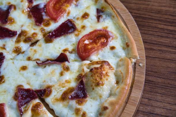 A close-up image of a pizza with melted cheese, tomato slices, and meat on a wooden board.