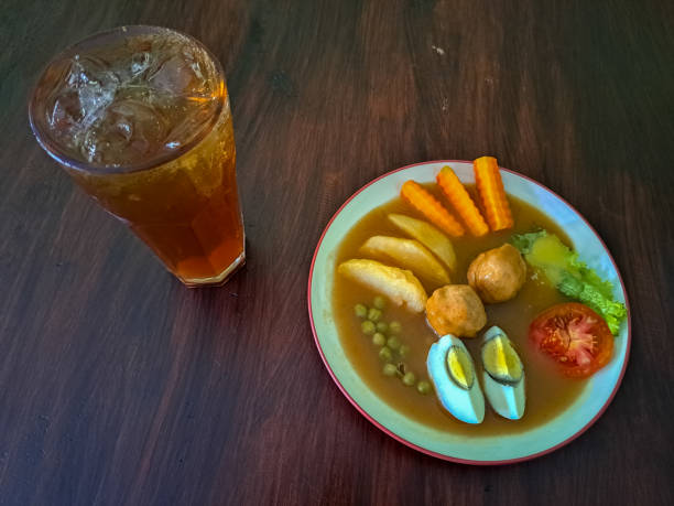 Tasty Bestik Glinding Or Beef Steak Is A Traditional Food From Indonesia. Serving With Beef Meat, Potato Wedges, Boiled Egg, Tomato, Lettuce, Green Peas And Carrot. Fresh Tea Iced Or Es Teh Segar In Glass. Food And Drink Menu. el sabroso bestik glinding o bistec de ternera es una comida tradicional de indonesia. servir con carne de res, gajos de papa, huevo hervido, tomate, lechuga, guisantes verdes y zanahoria. té fresco helado o es teh segar en vaso. menú de comida y bebida.